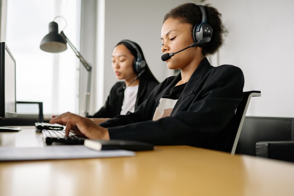 Duas atendentes de call center trabalhando em mesas em um ambiente de escritório com headsets.