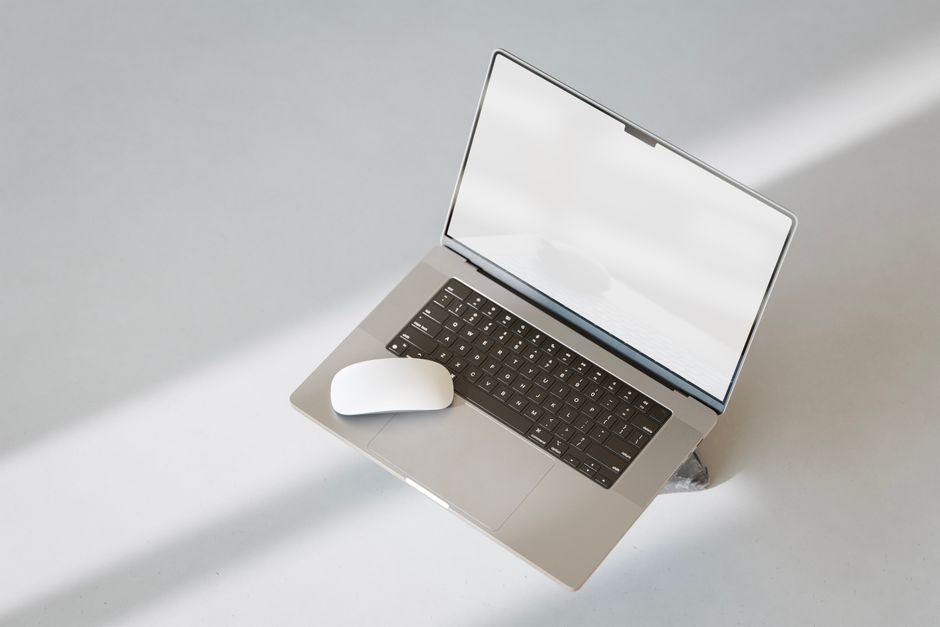 Um laptop moderno e um mouse sobre uma superfície limpa e branca, com uma estética minimalista.