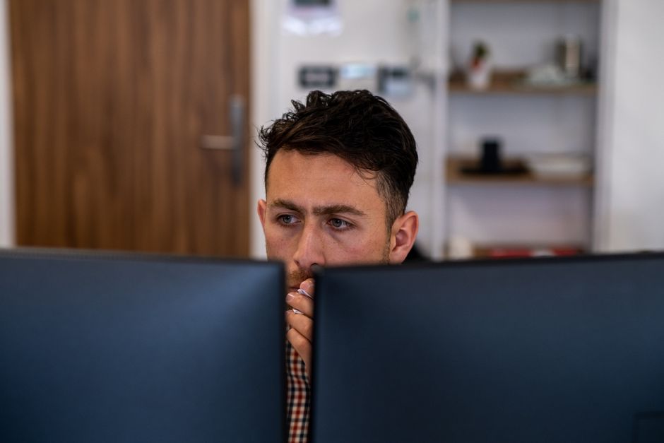 Homem profundamente focado no trabalho em sua mesa de escritório com monitores duplos.
