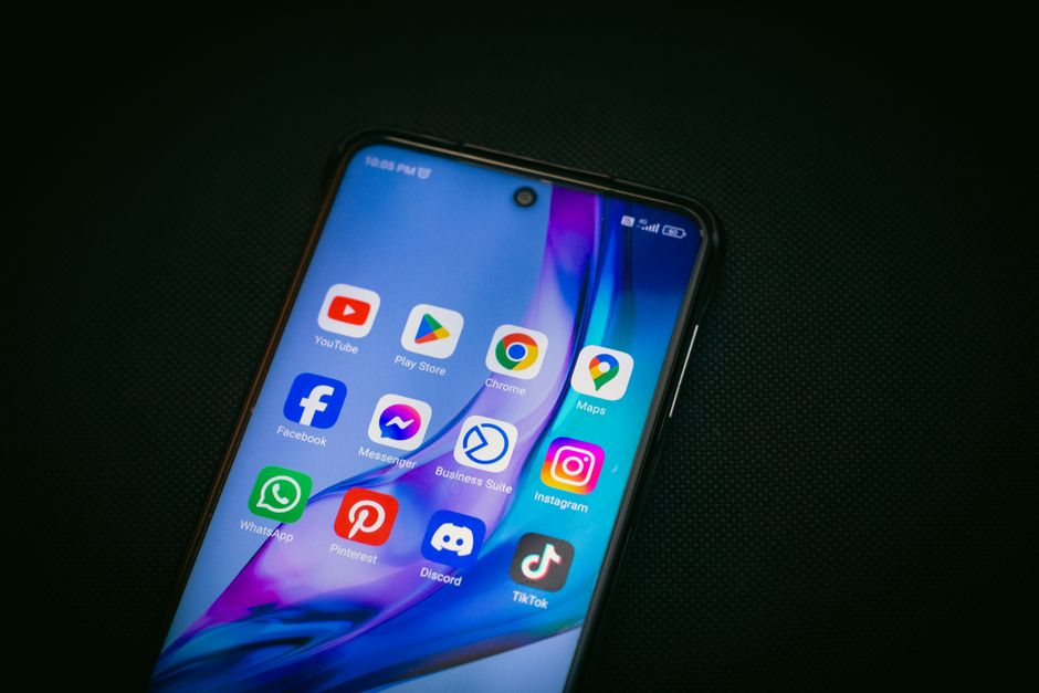 Close-up da tela de um smartphone mostrando ícones de aplicativos populares como YouTube, Maps e TikTok em um fundo preto.