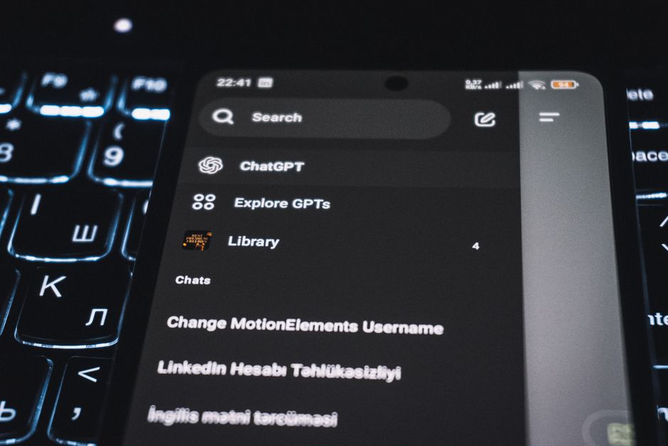 Close-up de um smartphone exibindo uma interface de app de chat com um teclado retroiluminado ao fundo.